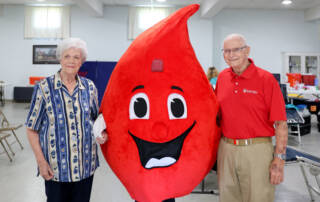 Man and woman standing next to Blood Drop mascot.