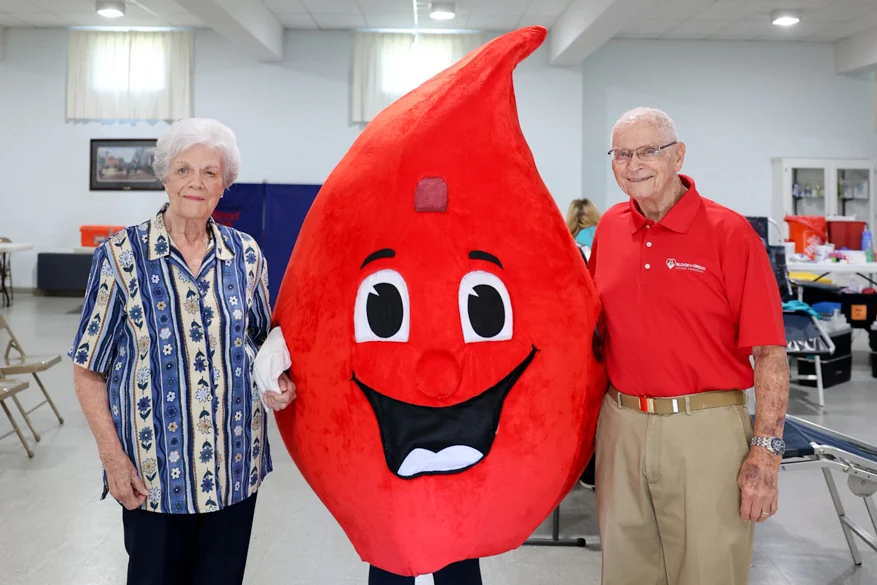 Man and woman standing next to Blood Drop mascot.