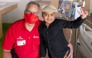 Man in mask and boy in hat smiling with hospital equipment behind them
