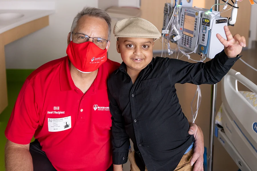 Man in mask and boy in hat smiling with hospital equipment behind them