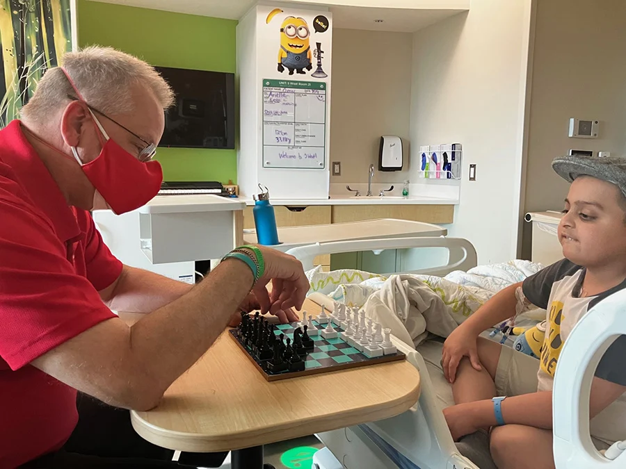 Man in mask and boy in hospital bed playing chess